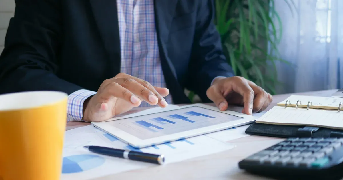 Dirigeant de PME analysant des graphiques de coûts sur une tablette, calculatrice à côté