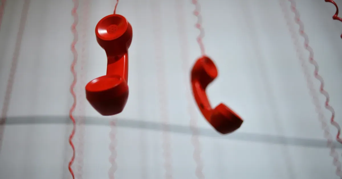 Combinés téléphoniques rouges suspendus à des fils, image du réflexe d'appeler le dépannage